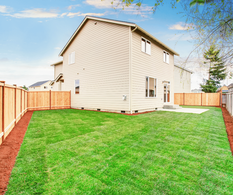 Standard subdivision house, pictured from the back corner of the yard and looking at the back of the house. A beautiful manicured and green lawn with a bark trim running around the perimeter.